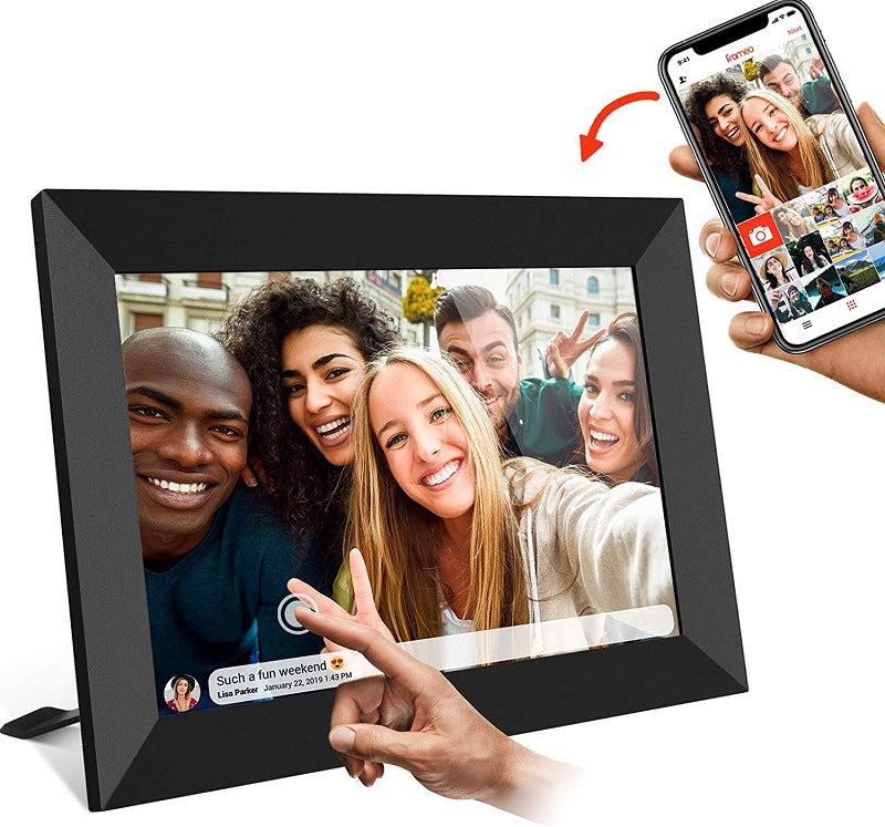 Digital photo frame displaying a selfie of four people, with a hand holding a phone showing a social media app interface.